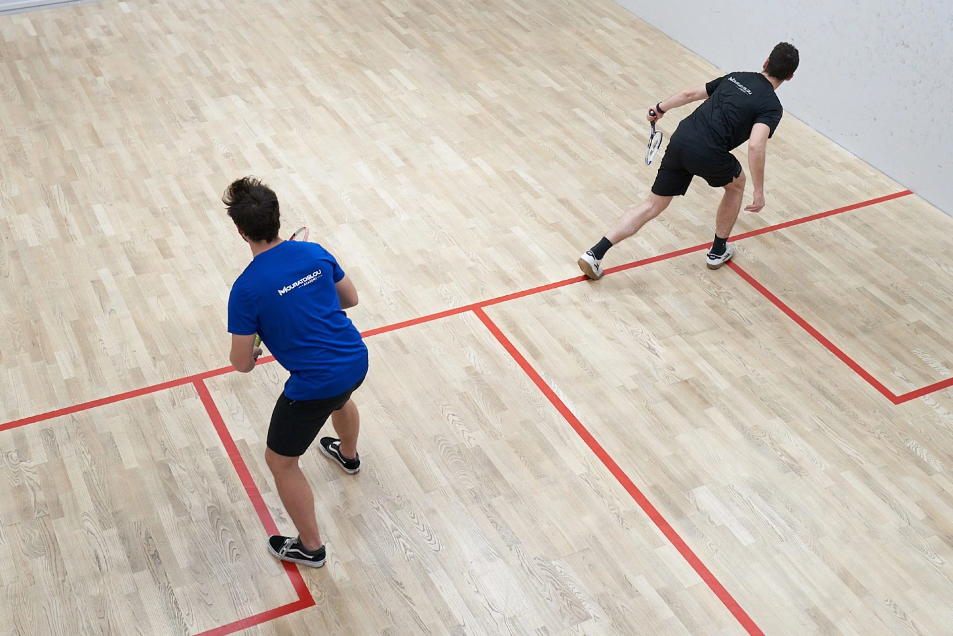 Two squash players practicing on an indoor wooden court
