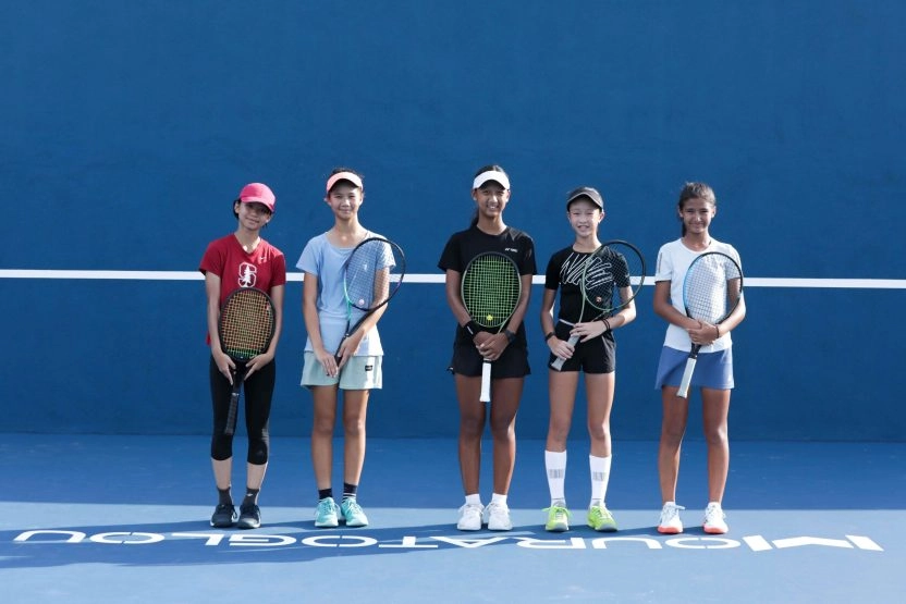 Group of junior tennis players standing with their rackets on a blue court