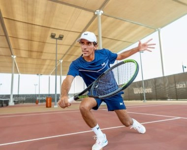 Tennis player performing a low forehand shot on a covered outdoor court.