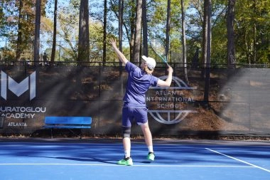 Young tennis player serving from behind on court at Mouratoglou Academy Atlanta