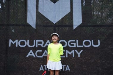 Jeune fille souriante debout devant les coupe-vent Mouratoglou à l'Académie Mouratoglou d'Atlanta