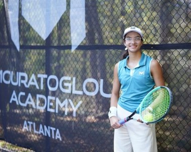 Young tennis player standing in front of a Mouratoglou windbreaker on court at Mouratoglou Academy Atlanta