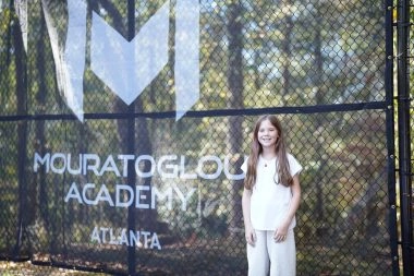 Young female tennis player standing in front of Mouratoglou windbreakers at Mouratoglou Academy Atlanta