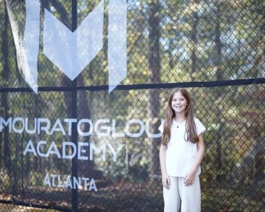 Young female tennis player standing in front of Mouratoglou windbreakers at Mouratoglou Academy Atlanta