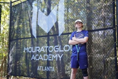 Jeune joueur de tennis debout devant les bâches Mouratoglou à l'Académie Mouratoglou d'Atlanta