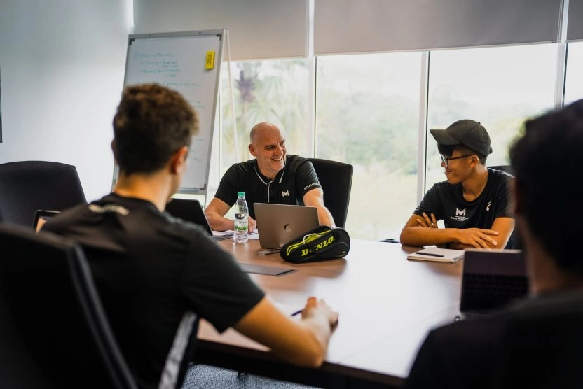 Coach leading a wellbeing and personal care meeting with students around a table