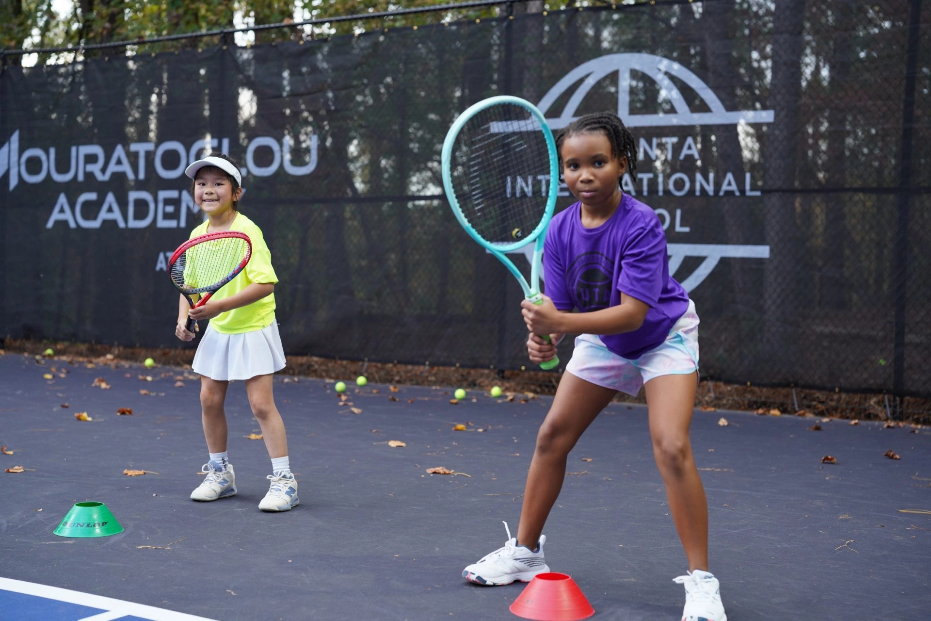 Two young tennis players training with their coach on court at Mouratoglou Academy Atlanta