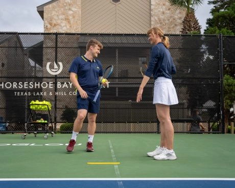 Two adults talking on a hard tennis court at Mouratoglou Tennis Center Horseshoe Bay.