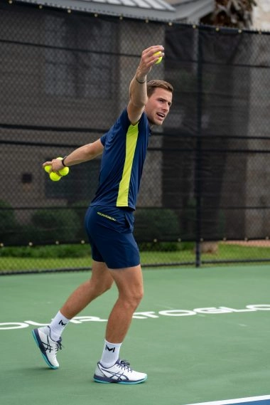 Un coach de tennis exécute un revers à une main sur un court extérieur au Mouratoglou Tennis Center à Horseshoe Bay.