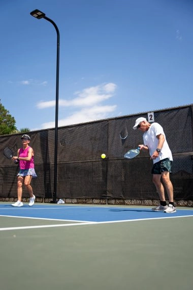 Two adults playing pickleball on an outdoor court at Mouratoglou Tennis Center Horseshoe Bay under sunny conditions.