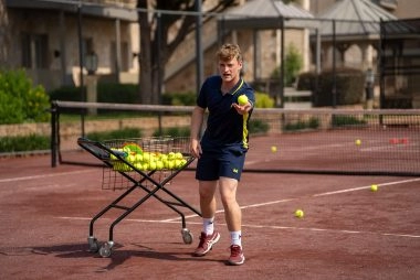 Tennis coach throwing a ball on a clay court at Mouratoglou Tennis Center Horseshoe Bay.