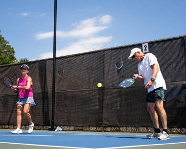 Deux adultes jouent en double sur un court de pickleball extérieur au Mouratoglou Tennis Center à Horseshoe Bay sous le soleil.