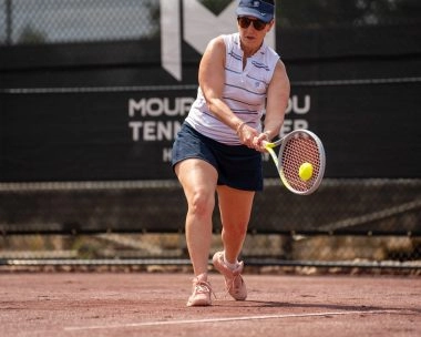 A woman hitting a backhand on a red clay tennis court at Mouratoglou Tennis Center Horseshoe Bay.