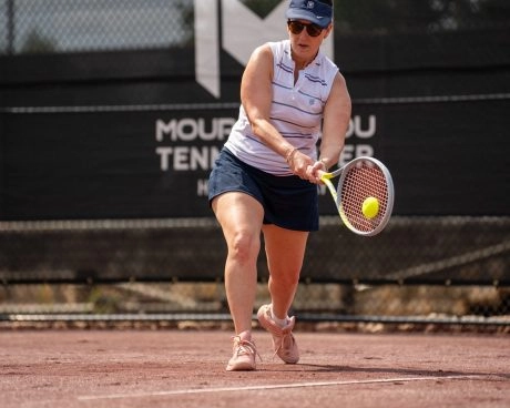A woman hitting a backhand on a red clay tennis court at Mouratoglou Tennis Center Horseshoe Bay.