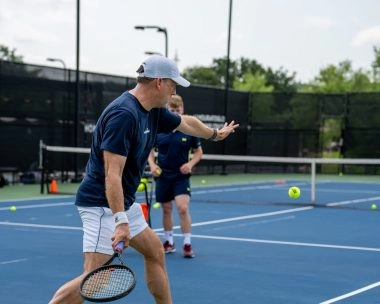 Un homme frappe un coup droit lors d’une leçon privée de tennis avec un coach sur un court extérieur au Mouratoglou Tennis Center à Horseshoe Bay.