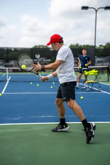 Un adulte réalise un revers à une main lors d’une leçon privée de tennis sur un court extérieur au Mouratoglou Tennis Center à Horseshoe Bay.