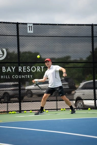 Un adulte frappe un coup droit lors d’une leçon privée de tennis avec un coach sur un court extérieur au Mouratoglou Tennis Center à Horseshoe Bay.