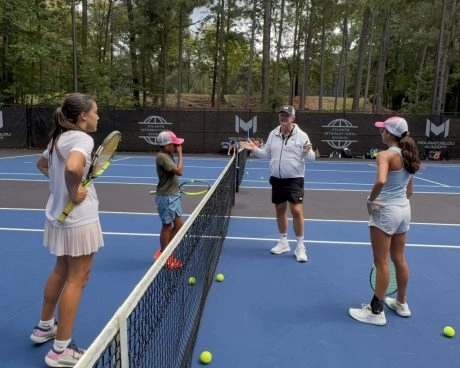 Three children at the net of a tennis court listening to their coach giving advice at Mouratoglou Academy Atlanta.