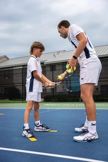 Un enfant s’entraîne au tennis avec un coach sur un court extérieur à Horseshoe Bay, Mouratoglou Tennis Center.