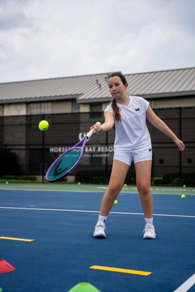 Une jeune fille joue au tennis sur un court extérieur à Horseshoe Bay, Mouratoglou Tennis Center.