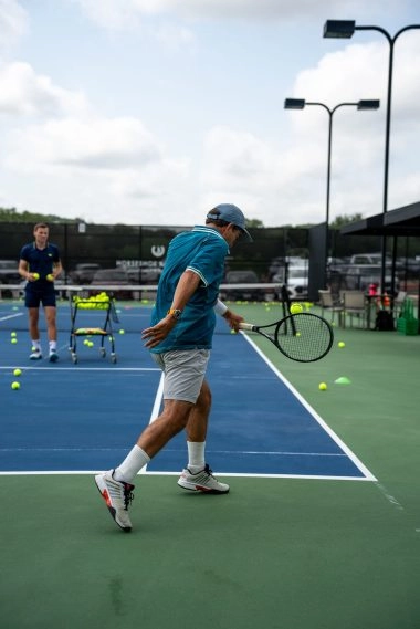 A man hitting a backhand on a hard tennis court at Mouratoglou Tennis Center Horseshoe Bay.