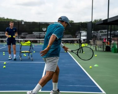A man hitting a backhand on a hard tennis court at Mouratoglou Tennis Center Horseshoe Bay.