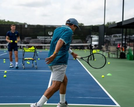 A man hitting a backhand on a hard tennis court at Mouratoglou Tennis Center Horseshoe Bay.