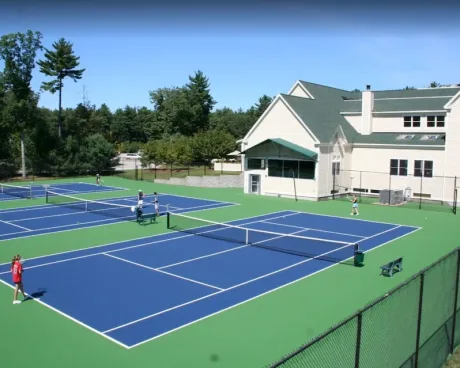Outdoor tennis courts beside a clubhouse with players practicing