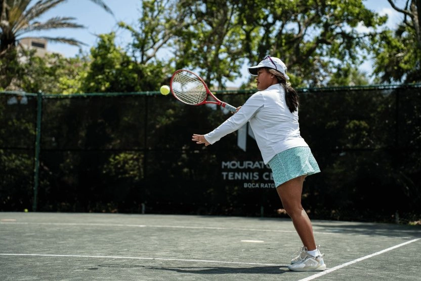 Adult woman hitting a tennis shot on an outdoor court at Mouratoglou Tennis Center Boca Raton.
