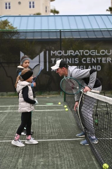 Tennis coach greeting two young players on court at Mouratoglou Tennis Center Amelia Island. Image description: