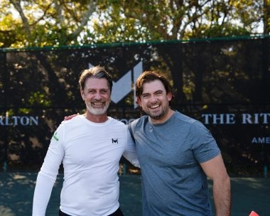 Patrick Mouratoglou posing with a player in front of Mouratoglou-branded windbreakers at Amelia Island.