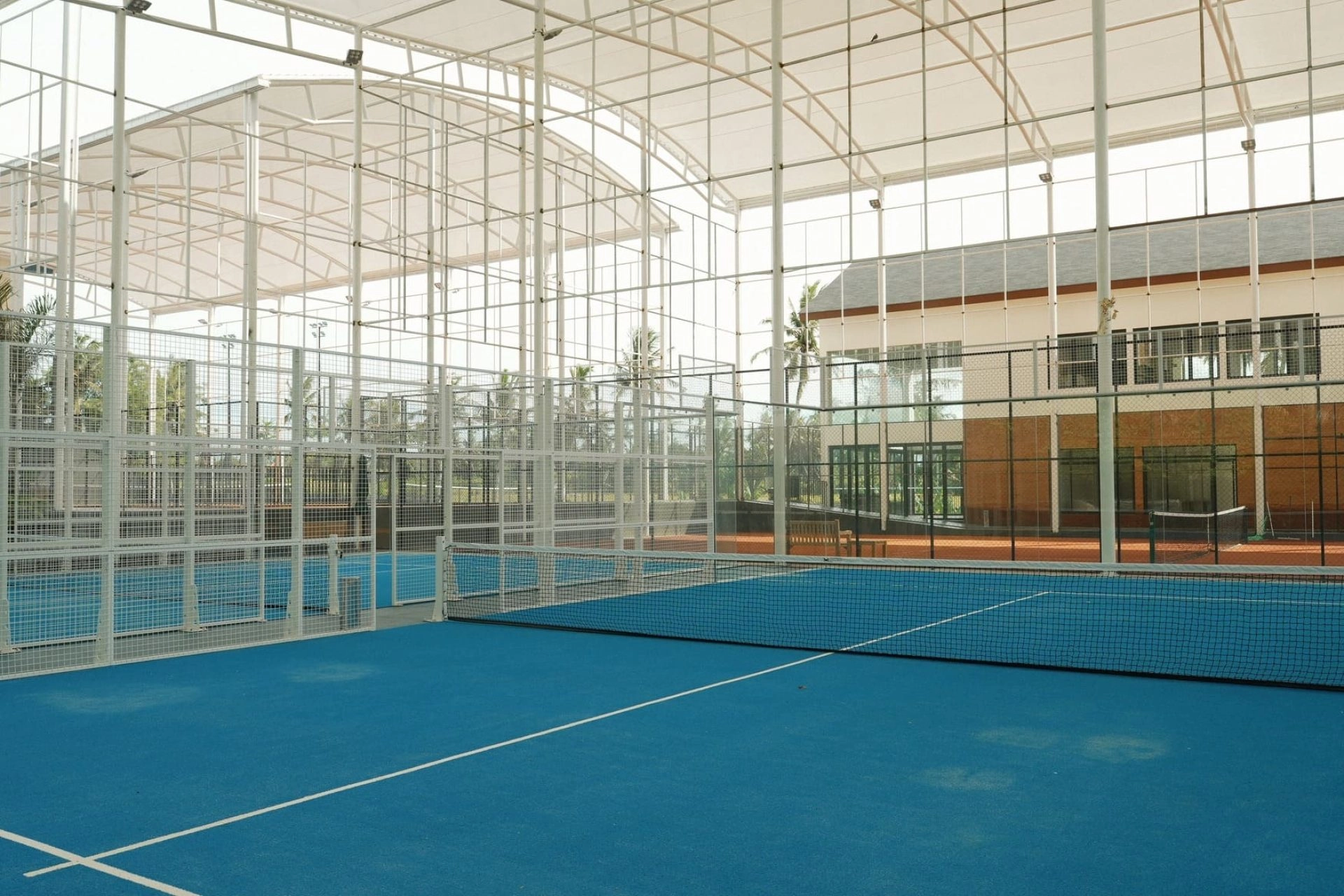 Terrain de padel semi-intérieur au Mouratoglou Tennis Center Bali avec un paysage tropical visible à l'extérieur.