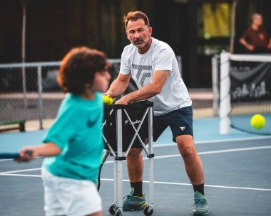 Tennis coach training a child on a blue court at Mouratoglou Tennis Center Calatrava