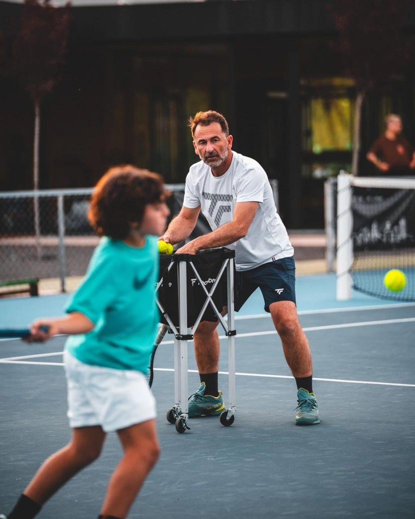 Tennis coach training a child on a blue court at Mouratoglou Tennis Center Calatrava