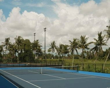 Outdoor hard tennis court at Mouratoglou Tennis Center Bali with palm trees and tropical landscape in the background.