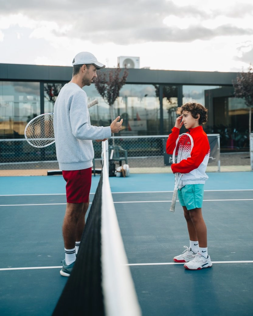 Tennis coach instructing a young player on an outdoor court at Mouratoglou Tennis Center Calatrava.