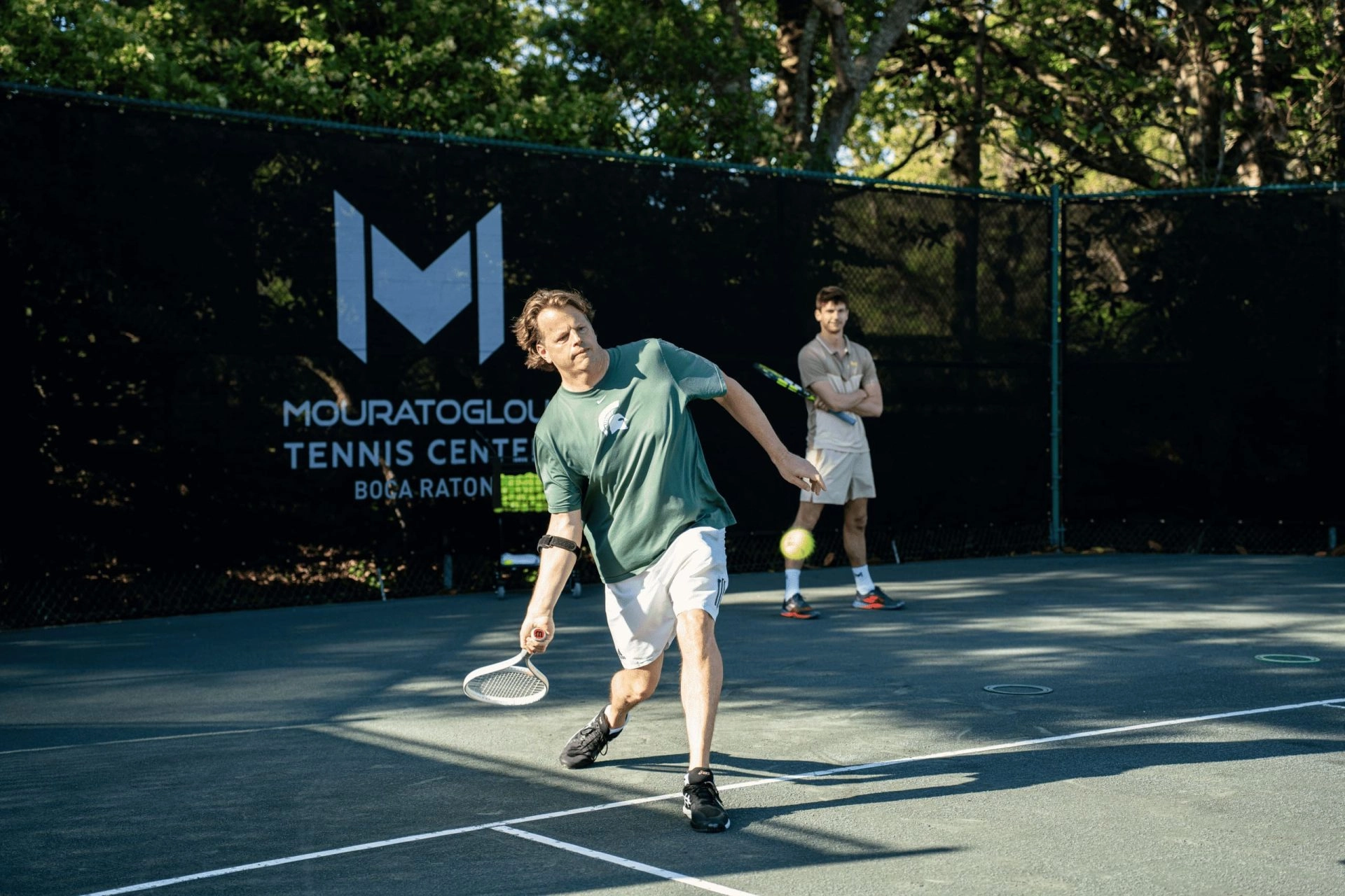 Coach giving a private tennis lesson to a player on an outdoor court at Mouratoglou Tennis Center Boca Raton.