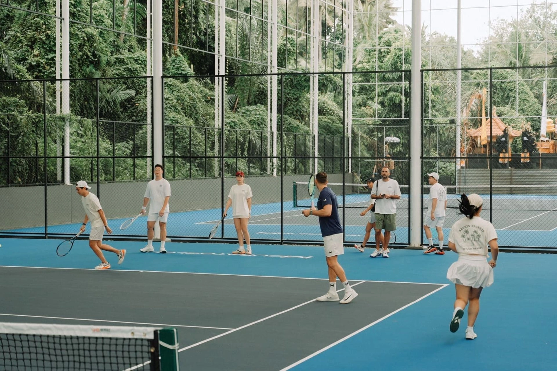Entraînement en groupe du camp de tennis pour adultes sur les courts de tennis en dur semi-intérieurs du Mouratoglou Tennis Center Bali avec l'entraîneur et les joueurs en action.