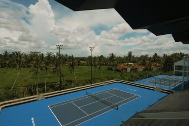Outdoor hard tennis court with covered seating and second court at Mouratoglou Tennis Center Bali with tropical greenery in the background.