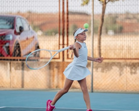 A young girl hitting a tennis shot on an outdoor court at Mouratoglou Tennis Center Calatrava.
