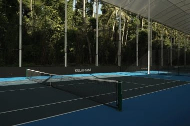 Covered hard tennis court at Mouratoglou Tennis Center Bali with roof structure and tropical foliage in the background.