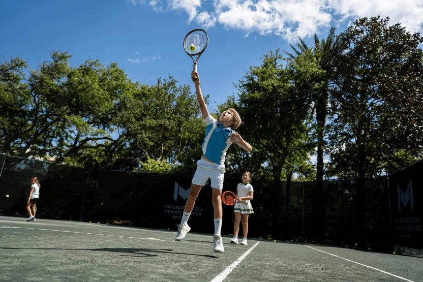 Young junior tennis players training together on an outdoor court at Mouratoglou Tennis Center Boca Raton.