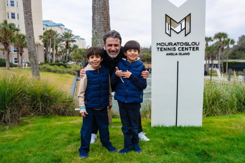 Patrick Mouratoglou posing with two children in front of the Mouratoglou totem at Amelia Island.