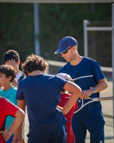 Tennis coach training multiple children on blue outdoor courts at Mouratoglou Tennis Center Calatrava