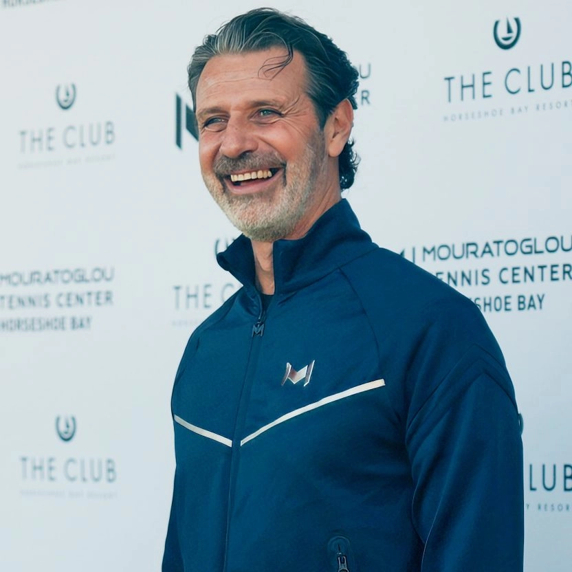 Patrick Mouratoglou smiling at the Mouratoglou Tennis Center Horseshoe Bay event with branded backdrop.