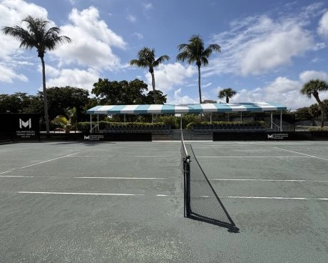 Outdoor tennis courts at Mouratoglou Tennis Center Boca Raton in Florida with players and palm trees in a sunny setting.