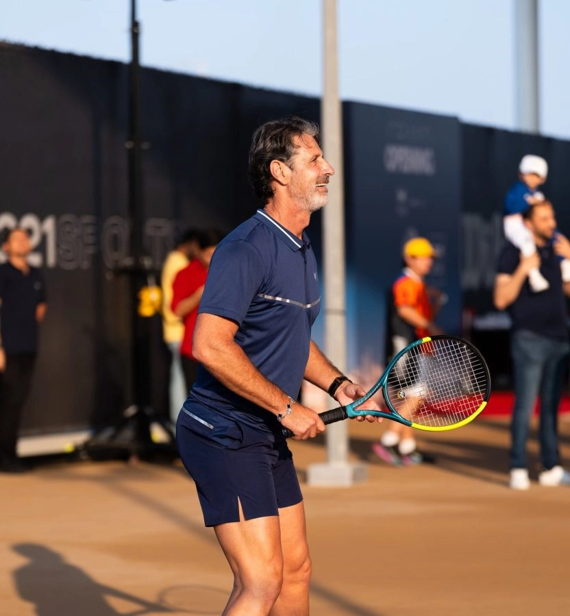 Patrick Mouratoglou smiling in ready position holding a tennis racket on a court at Mouratoglou Tennis Center Hudayriyat Island in Abu Dhabi.