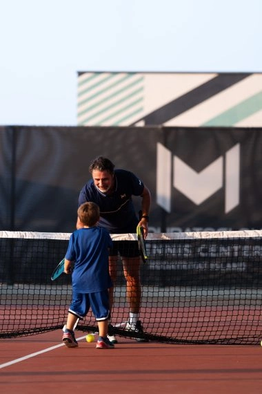 Patrick Mouratoglou coaching a child on a tennis court at Mouratoglou Tennis Center Hudayriyat Island in Abu Dhabi.
