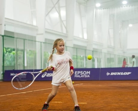 Young girl hitting a tennis shot on an indoor clay court at Mouratoglou Academy Malaysia on the campus of Epsom College in Malaysia.
