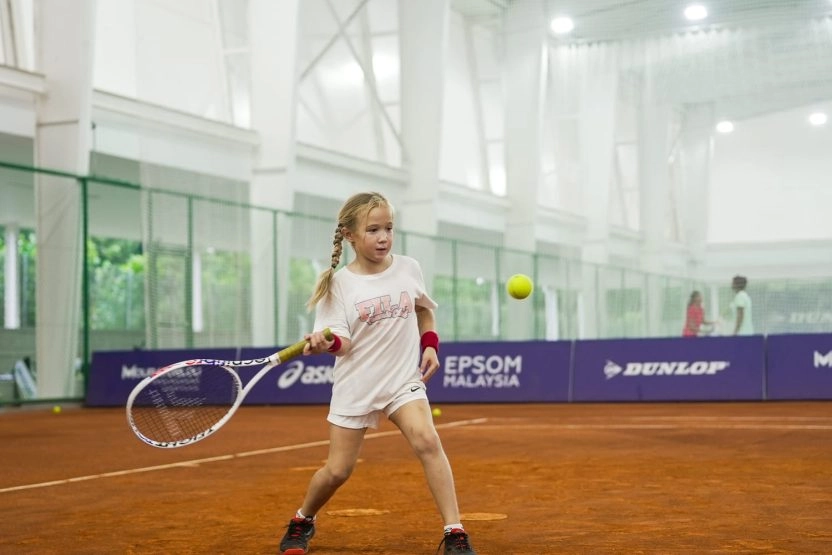 Young girl hitting a tennis shot on an indoor clay court at Mouratoglou Academy Malaysia on the campus of Epsom College in Malaysia.